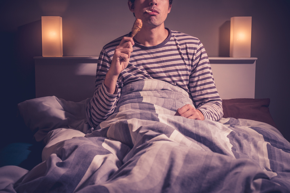 Homme mangeant un pilon de poulet dans son lit