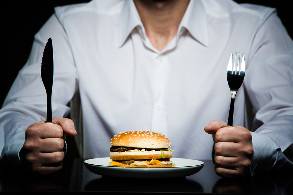 Homme tenant ses couverts devant un hamburger