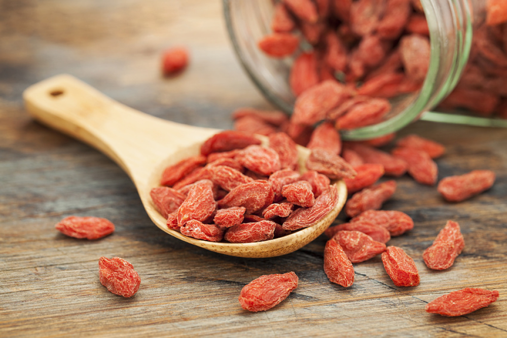 Bocal de baies de goji déversées sur une cuillère en bois posée sur une table