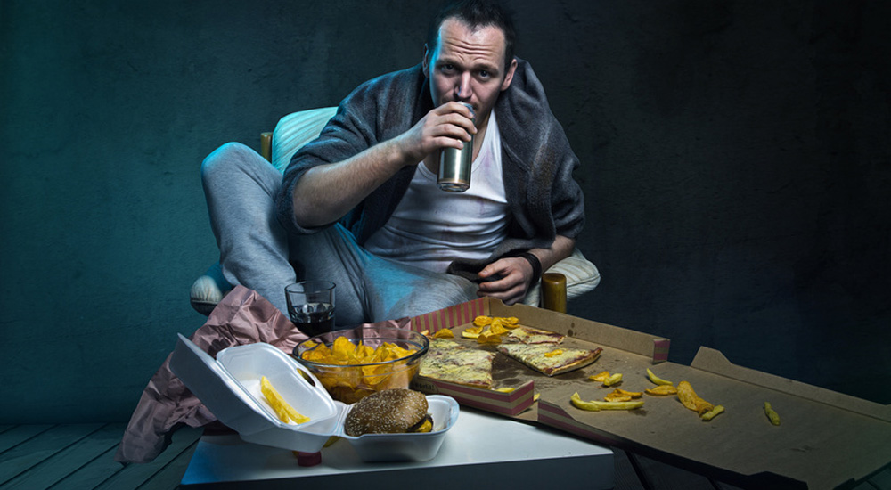 Homme mangeant de la junk food devant sa télé