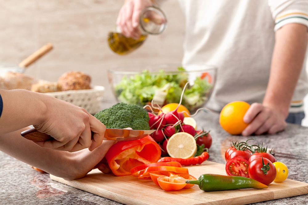 Deux personnes coupant des légumes et assaisonnant une salade